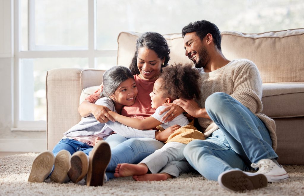 family of 4, hugging on the floor in front of couch, happy.